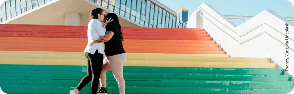 Un couple s'embrasse sur un escalier peint au couleurs de l'arc-en-ciel